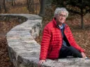 David Roberts seated outdoors on a stone wall by the Charles River