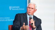 Mike Pence speaks into a microphone, gesturing, against a blue backdrop.
